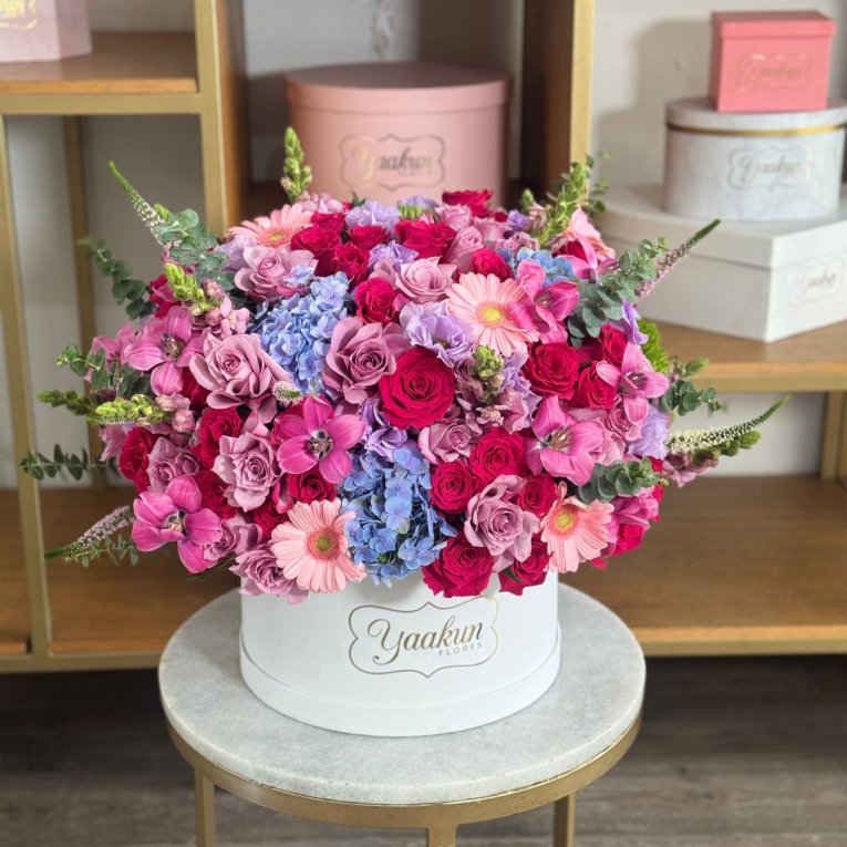 Caja circular blanca con 100 rosas en tonos, lilas, fucsias y azul