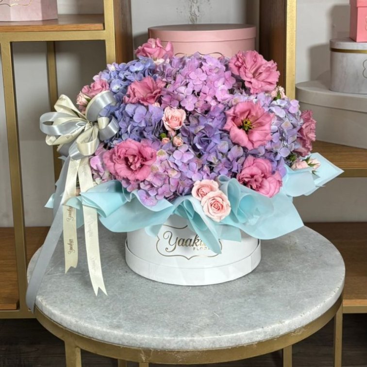 Caja circular mini blanca con hortensias lila, lisianthus rosa y baby rose