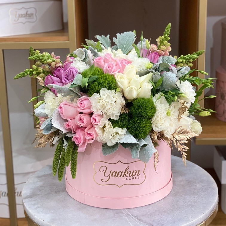 Caja circular rosita  con 75 rosas rosas y lilas, follajes y flores finas toques dorados
