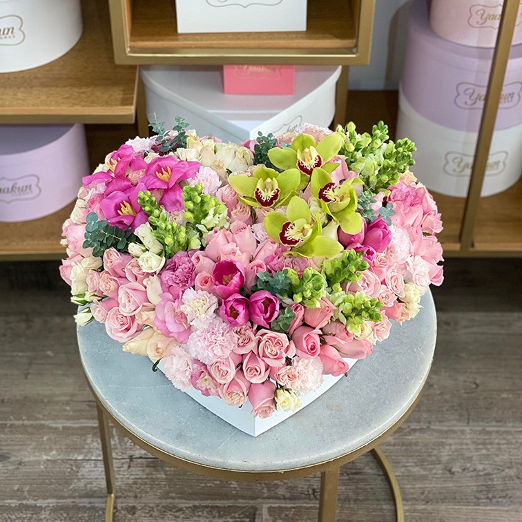 Caja corazón blanca c/t con 125 rosas, tulipanes, lisianthus perritos, baby rose y toques de orquídea cymbidium verde