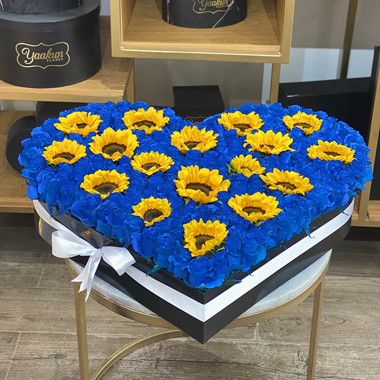 Caja corazón con rosas azules y girasoles con moño blanco